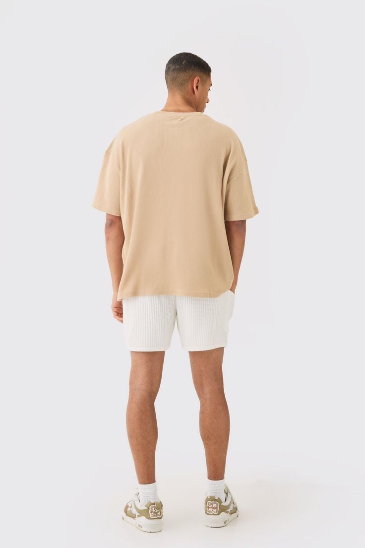 Back view of man wearing beige oversized t-shirt and white shorts with casual sneakers